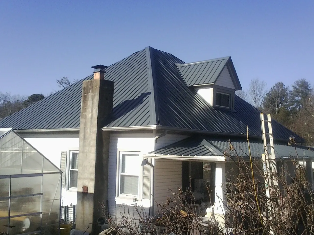 Dark blue standing seam metal roof on a white farmhouse with dormer — Slate & Tile Roof Repair by Roofing Brothers in Roberts