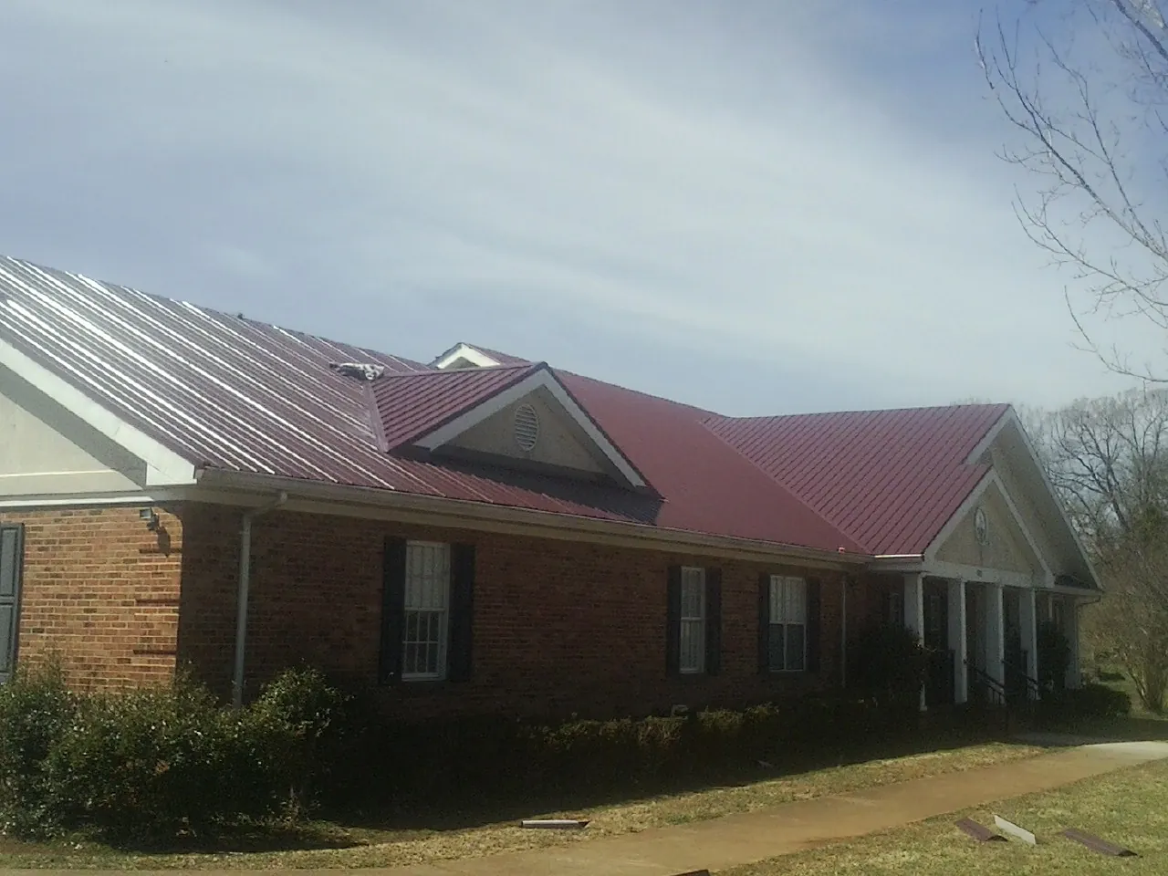 Red metal roof with gabled entries on a long brick building, from a Hail Damage Roof Repair job in Roberts
