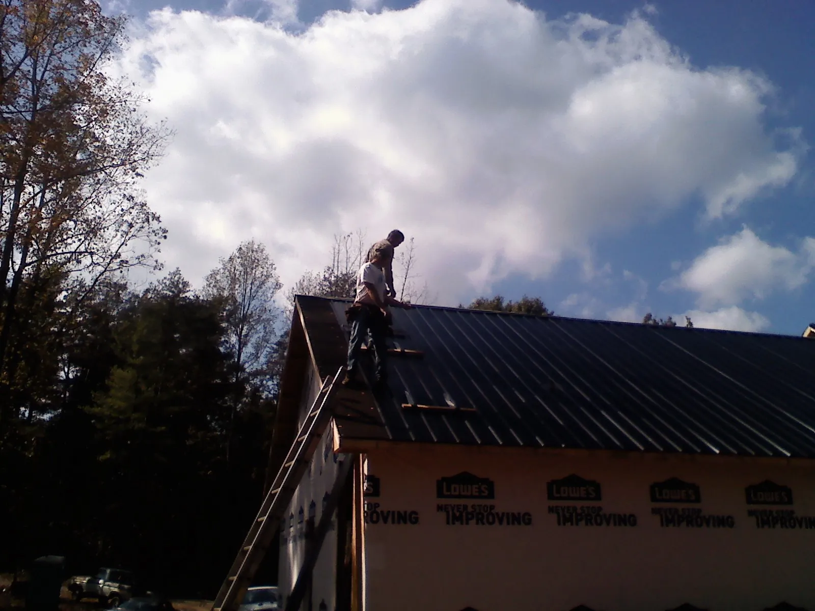 Roofer fastening dark metal panels high against a cloudy sky, from a Roof Inspection job in Roberts